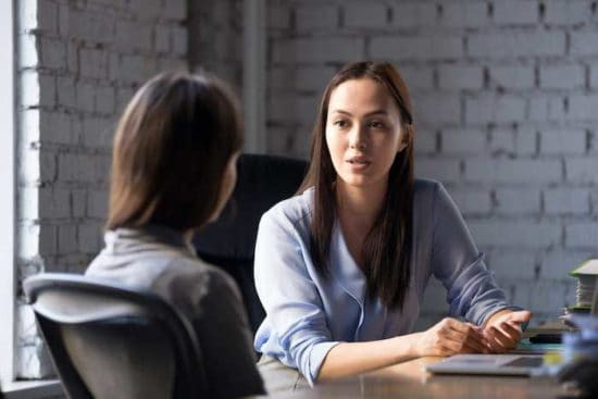 Hai phụ nữ trao đổi ý kiến bên bàn ăn gỗ với tường gạch tạo nên không gian ấm cúng