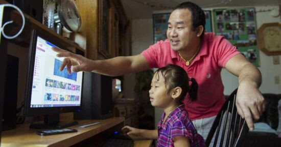 Người cha và con gái cùng sử dụng máy tính trên bàn làm việc hiện đại, tạo không gian học tập và kết nối