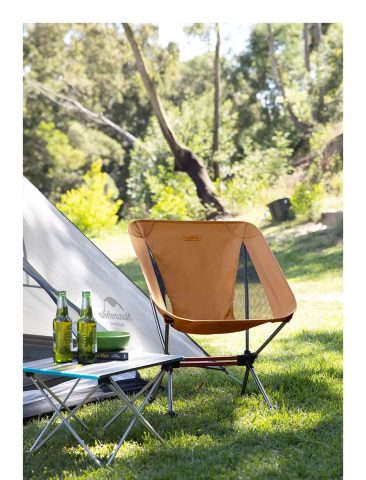 Người đàn ông đang ngồi trên ghế du lịch gấp gọn Naturehike màu xanh lính thoải mái bên bờ sông