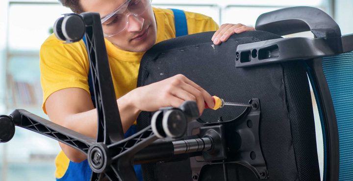 Người dùng đang siết chặt các ốc vít dưới mâm ghế để khắc phục tình trạng ghế xoay bị ngửa ra sau hoặc lung lay.